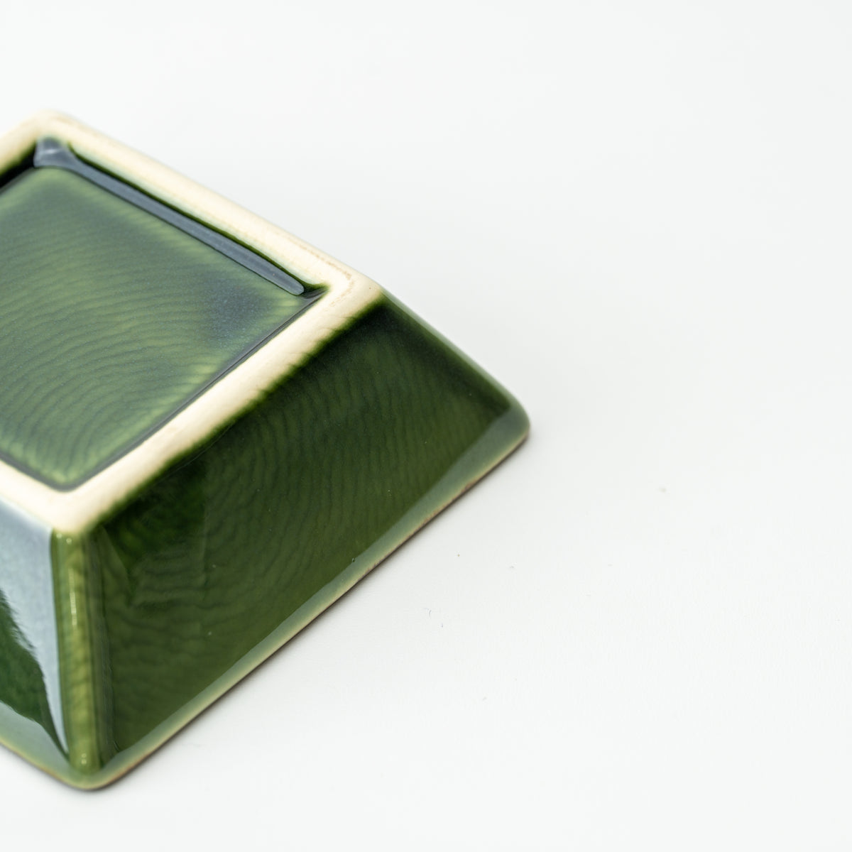 Underside corner of a green Mino bowl, showing the pale square foot and glossy sloping sides.