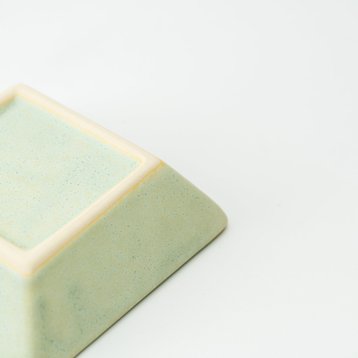 Underside corner of a pale green Mino bowl with a cream-colored square foot.