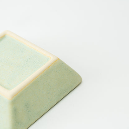 Underside corner of a pale green Mino bowl with a cream-colored square foot.