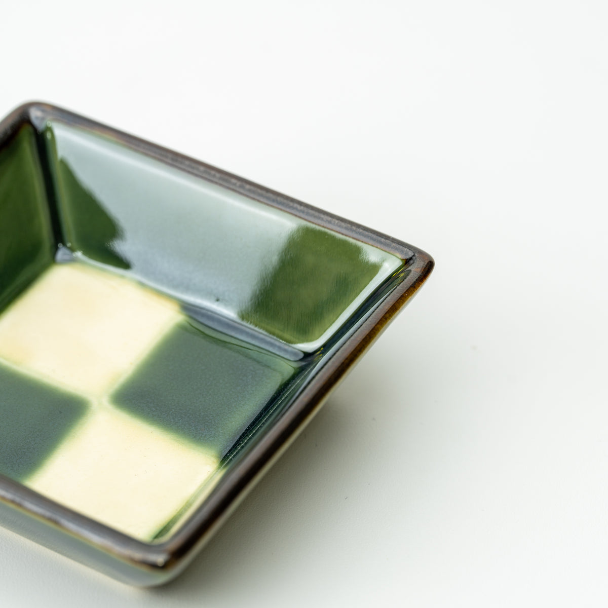 Close-up of a green-and-cream checkerboard Mino bowl's glossy interior and dark rim.