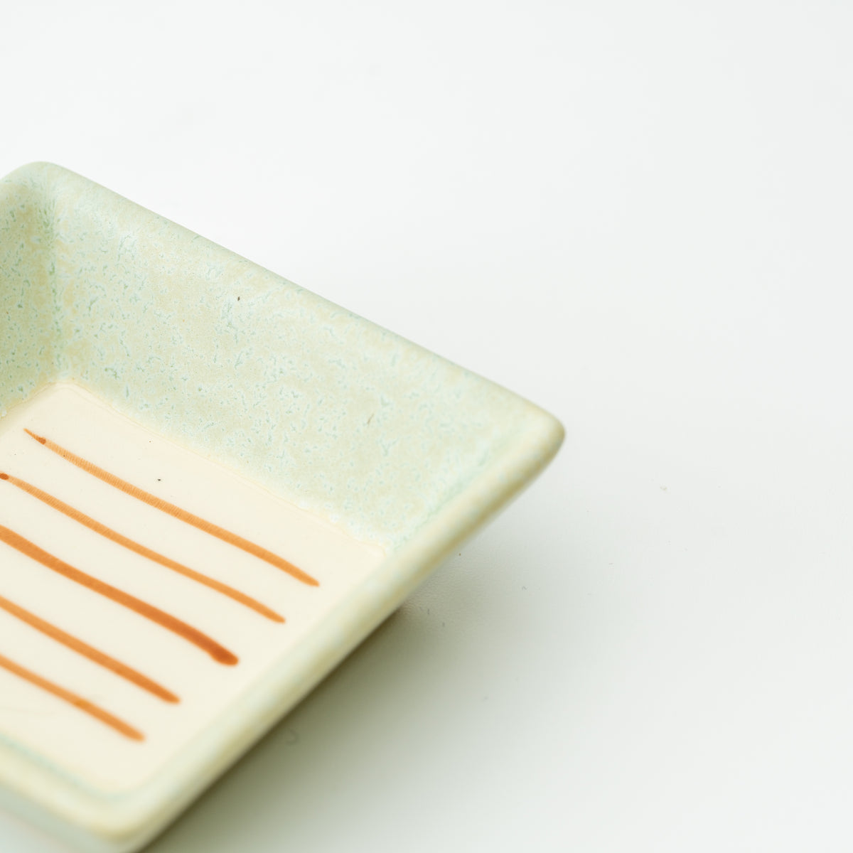 Detail of a pale green Mino bowl with parallel orange lines across its cream interior.