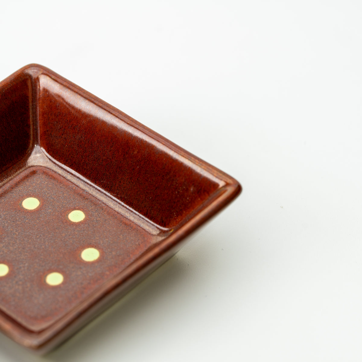 Detail of a reddish-brown Mino bowl with small pale dots inside its square base.