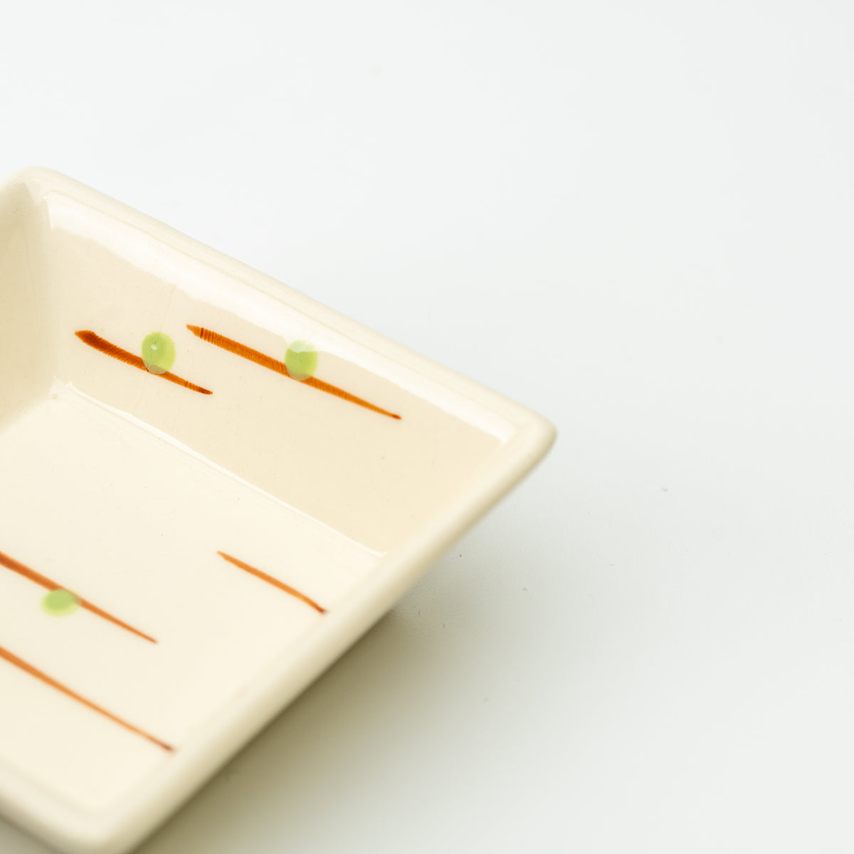 Close-up of a cream Mino bowl decorated with thin orange strokes and small green dots.