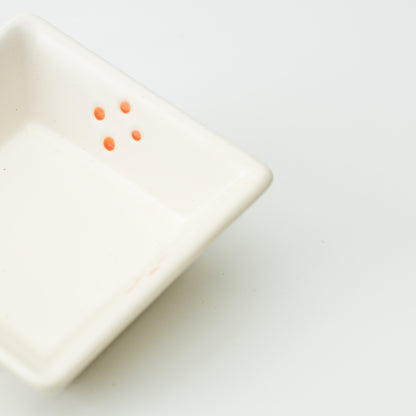 Detail of small orange dot clusters inside a white square Mino bowl.