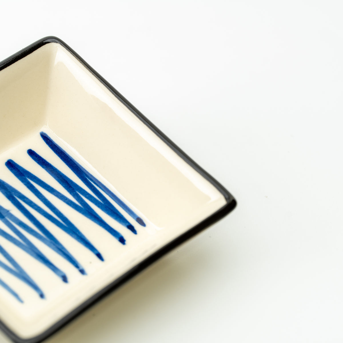 Detail of intersecting blue lines inside a cream Mino bowl with a dark rim.