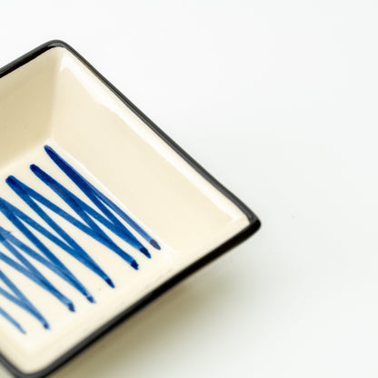 Detail of intersecting blue lines inside a cream Mino bowl with a dark rim.