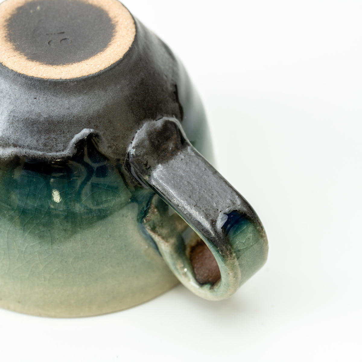 Underside and handle of the Hechimon Mosaic cup showing its foot ring and flowing dark glaze.