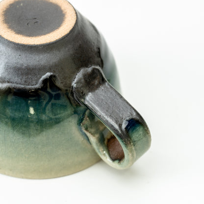 Underside and handle of the Hechimon Mosaic cup showing its foot ring and flowing dark glaze.