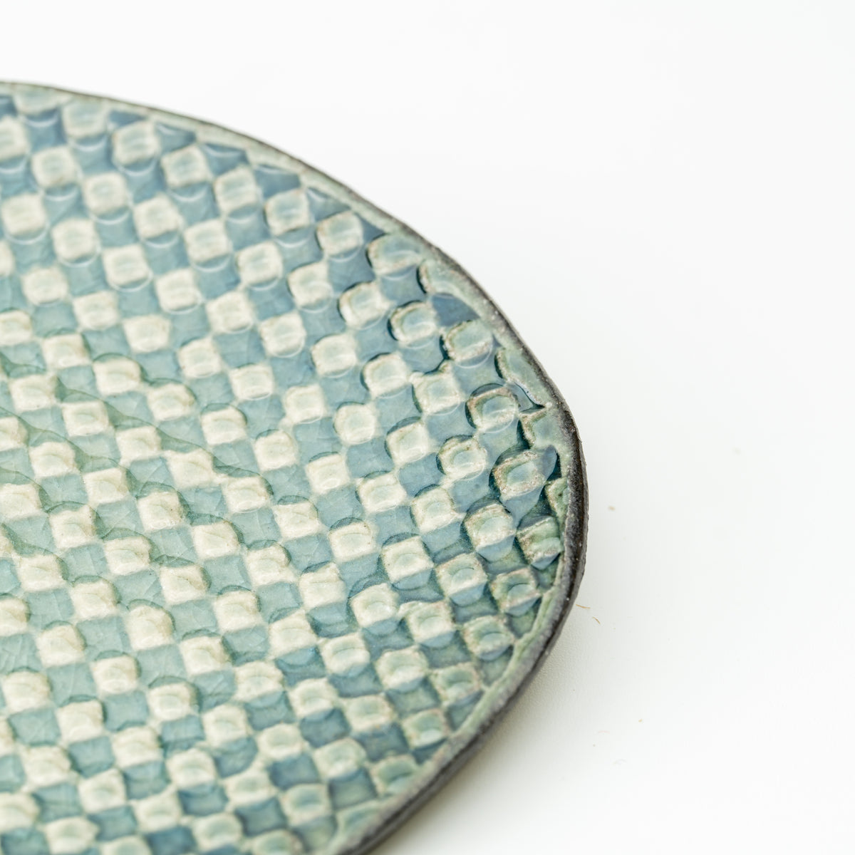 Detail of the Hechimon Mosaic saucer's pale green and teal checkered surface and dark rim.
