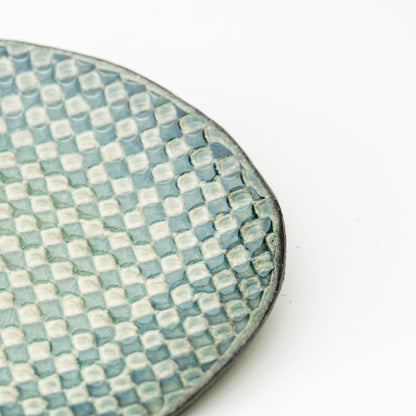 Detail of the Hechimon Mosaic saucer's pale green and teal checkered surface and dark rim.