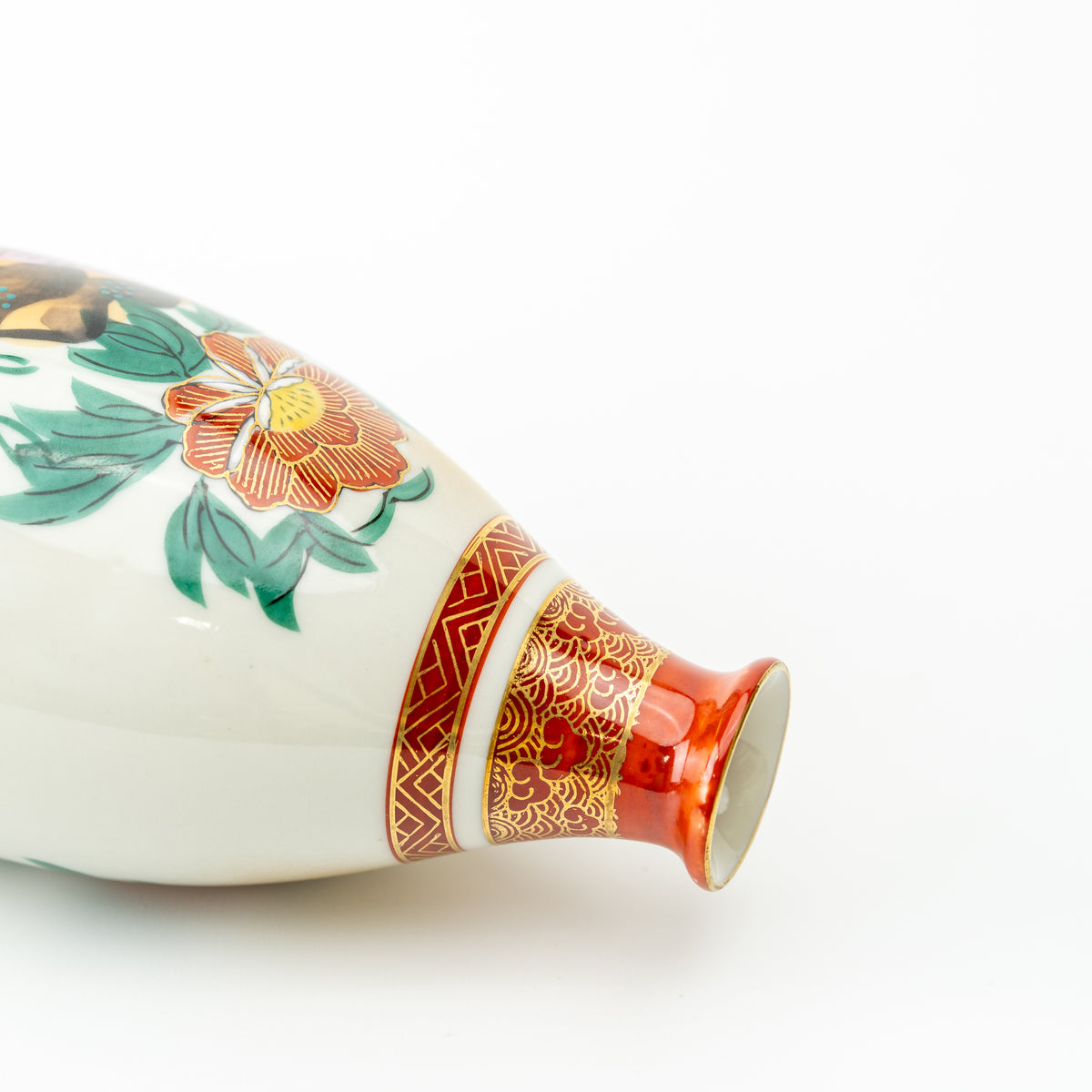 Close-up of the sake bottle lying on its side, showing a peony and red-and-gold neck decoration.