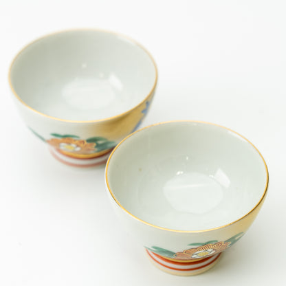 Two Kutani peacock and peony sake cups viewed from above, showing pale interiors and gold-colored rims.