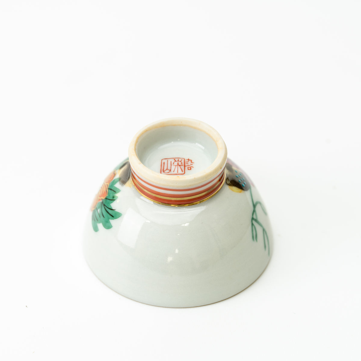 Underside of a Kutani sake cup, showing a red maker's mark inside its raised striped foot.