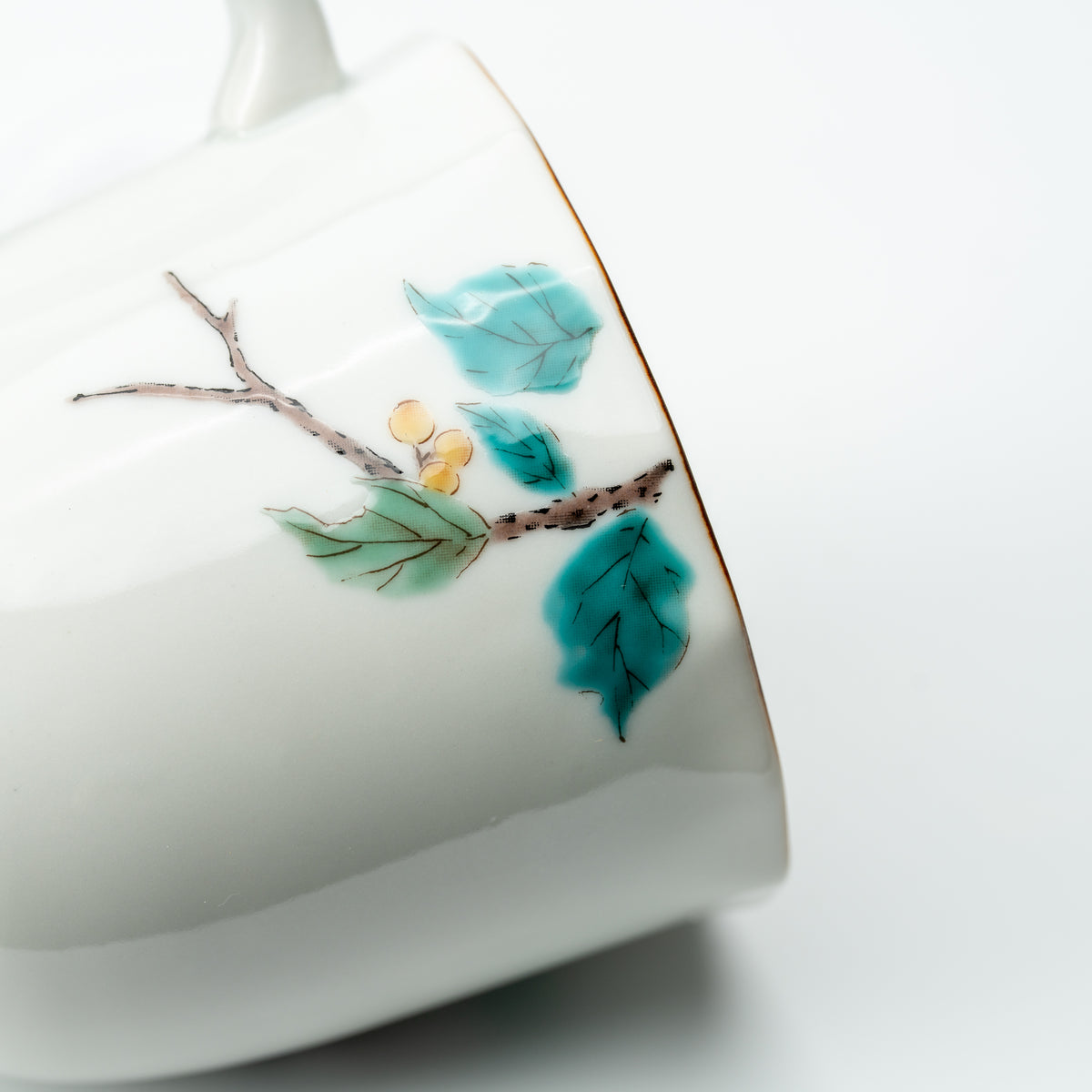 Close-up of turquoise leaves and a branch painted on the white Mejiro bird mug.