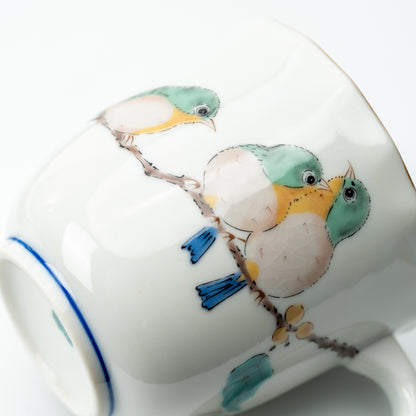 Close-up of green Mejiro birds perched together on a branch on the white mug.