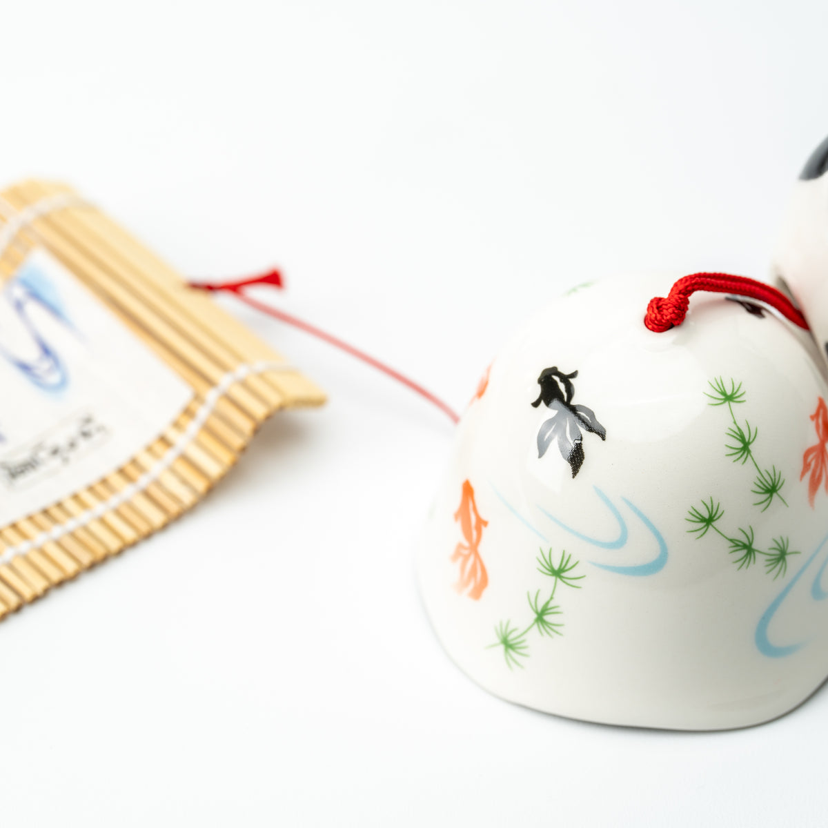 Close-up of the white wind-chime bell painted with goldfish, green plants and blue water ripples.