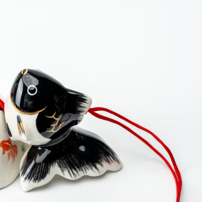 Close-up of the black goldfish wind chime's face and spreading tail beside its red cord.