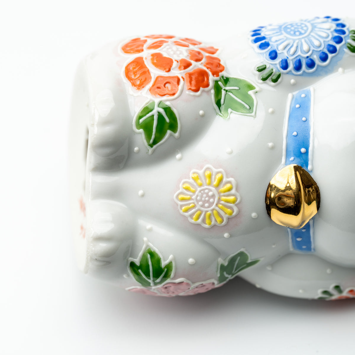 Close-up of raised orange, blue and yellow flowers and a gold-colored bell on the Hanazono lucky cat.