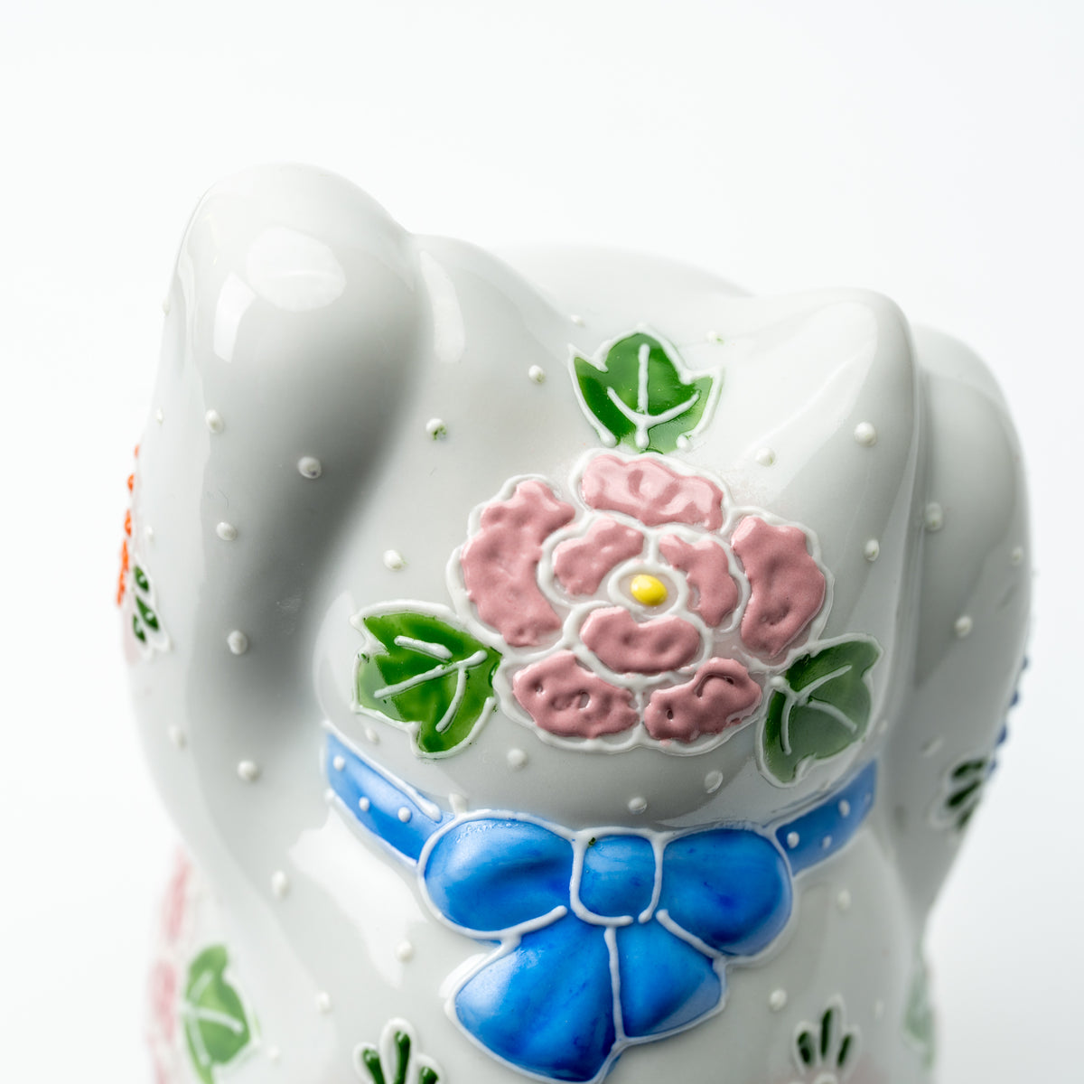 Close-up of the Hanazono lucky cat's back with a raised pink flower and blue bow.