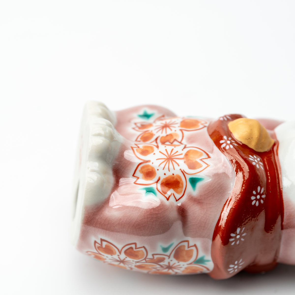 Side detail of the pink Sakura lucky cat showing cherry blossoms, a raised paw and gold-colored bell.