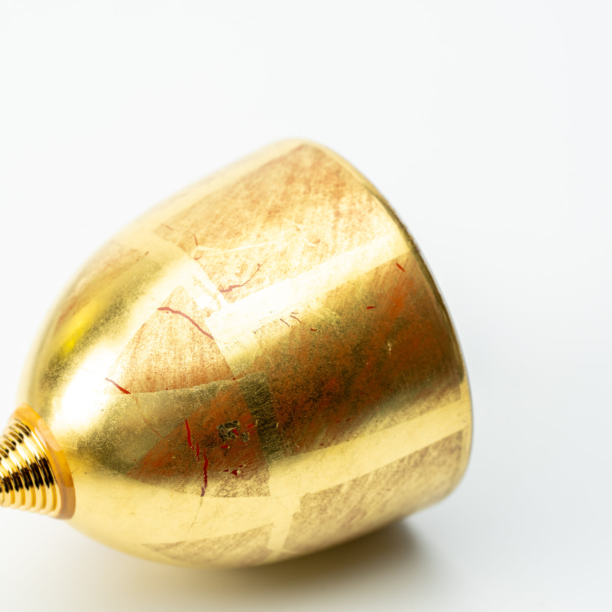 Side view of the gold leaf wine cup's rounded bowl, showing patches of red beneath the gold finish.