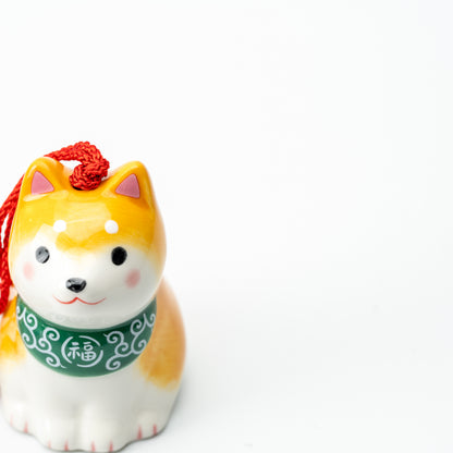 Front detail of the yellow Shiba wind chime with pink cheeks, a green bib and white paws.