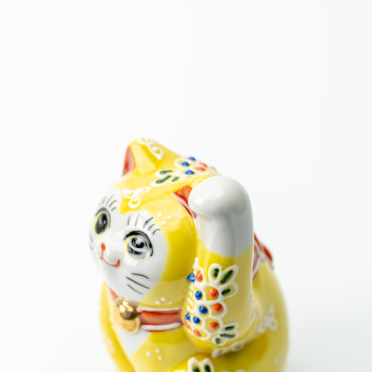 Close-up of the yellow Mori lucky cat's face and raised paw with colorful raised floral dots.