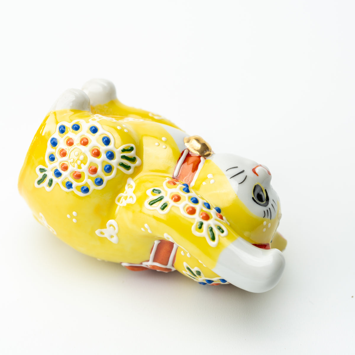 Yellow Mori lucky cat lying on its side to show raised floral decoration on its rounded body.
