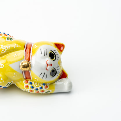 Close-up of the yellow Mori lucky cat's face, red collar and gold-colored bell while lying on its side.