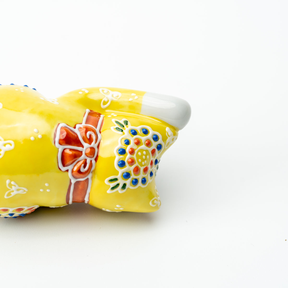 Detail of the red bow and colorful raised flower on the back of the yellow Mori lucky cat.