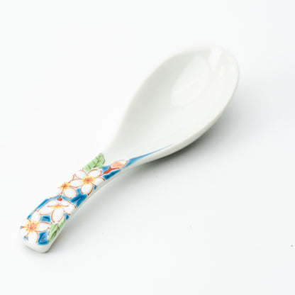 White Kutani soup spoon with small pale blossoms and green leaves on a blue-accented handle.