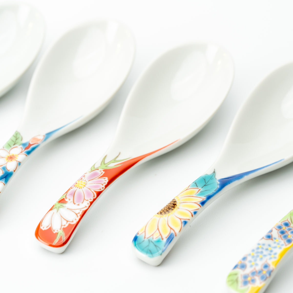 Angled detail of Kutani soup spoons with colorful floral handles and smooth white bowls.