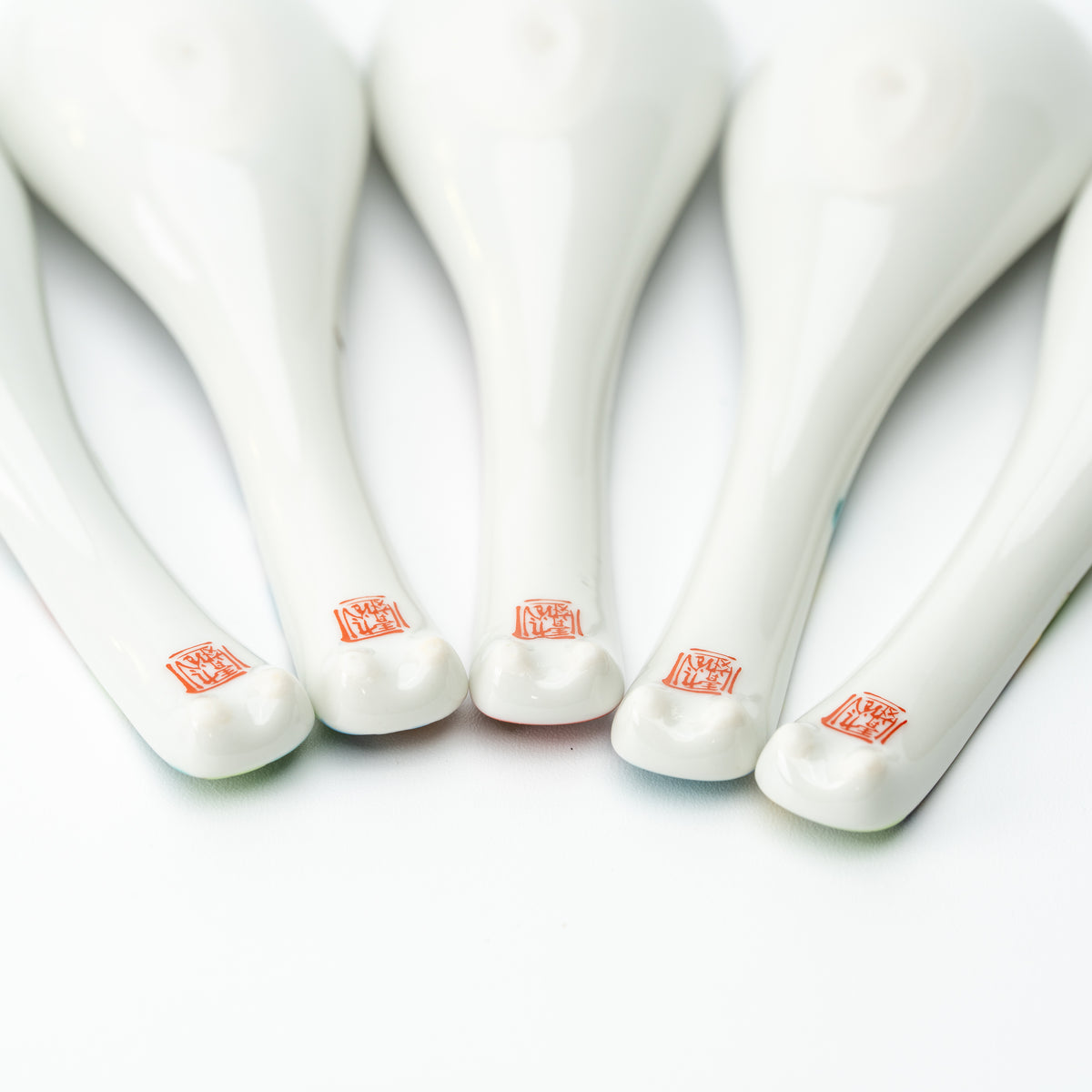 Undersides of five white Kutani soup spoons, showing red maker's marks near the handle tips.