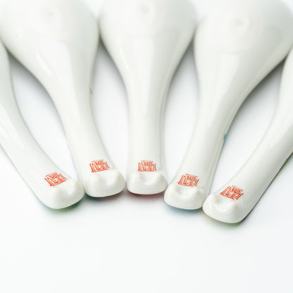 Undersides of five white Kutani soup spoons, showing red maker's marks near the handle tips.