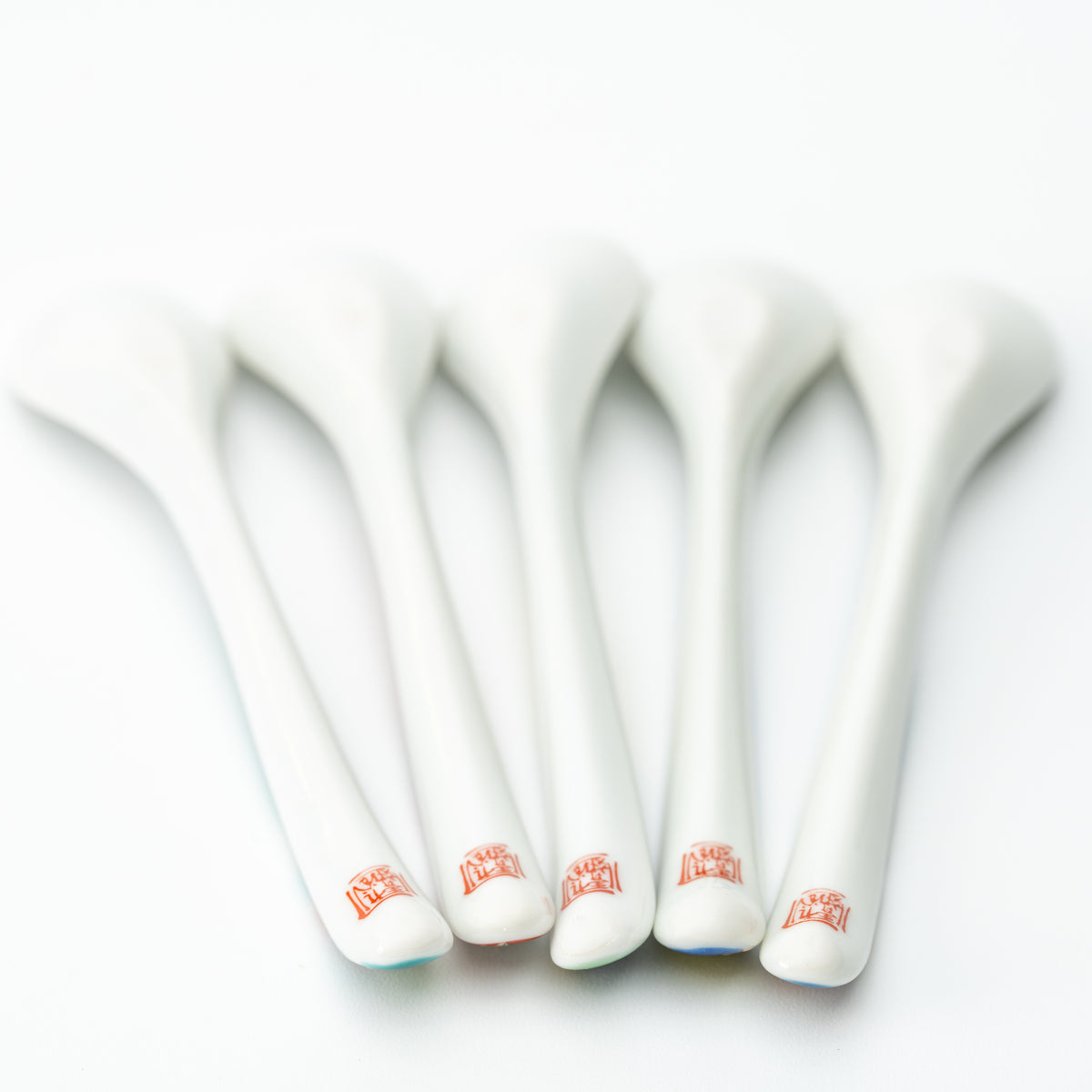Undersides of five Kutani tea spoons showing white backs and small red marks near the handle ends.