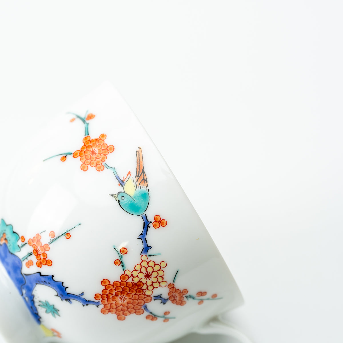 Close-up of a turquoise bird perched among orange plum blossoms on the white Arita cup.