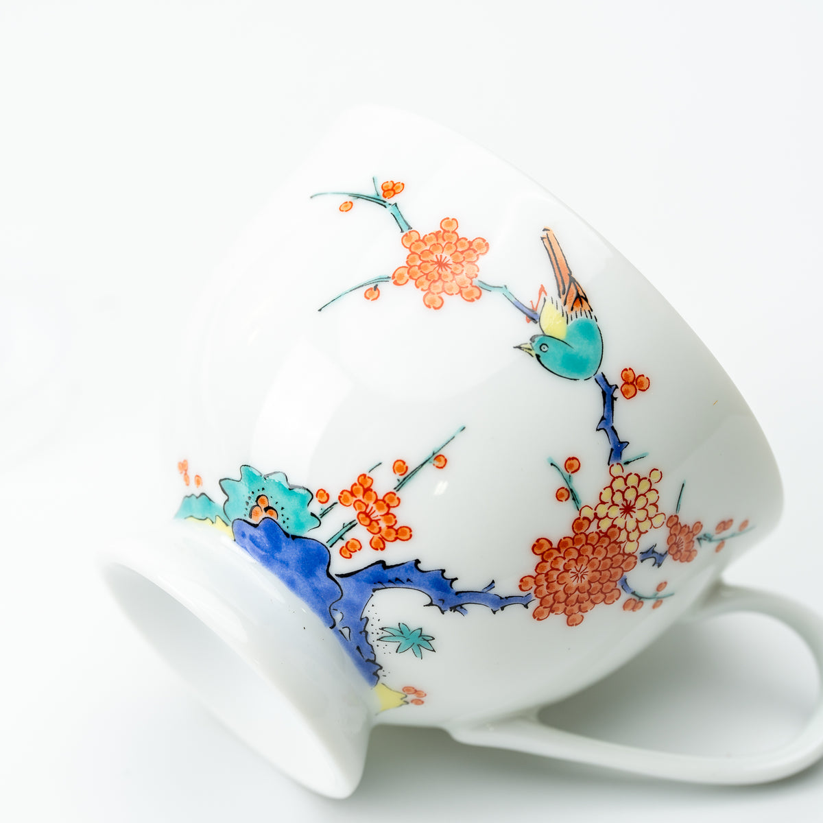 Plum blossom and bird cup resting on its side, showing orange flowers, a blue branch and curved white handle.