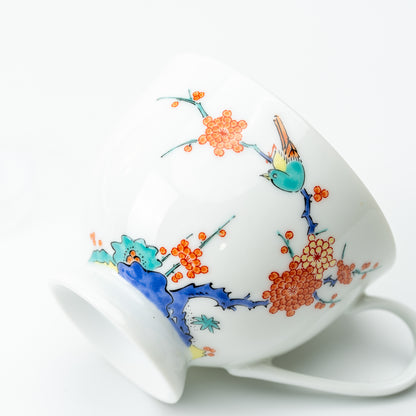 Plum blossom and bird cup resting on its side, showing orange flowers, a blue branch and curved white handle.