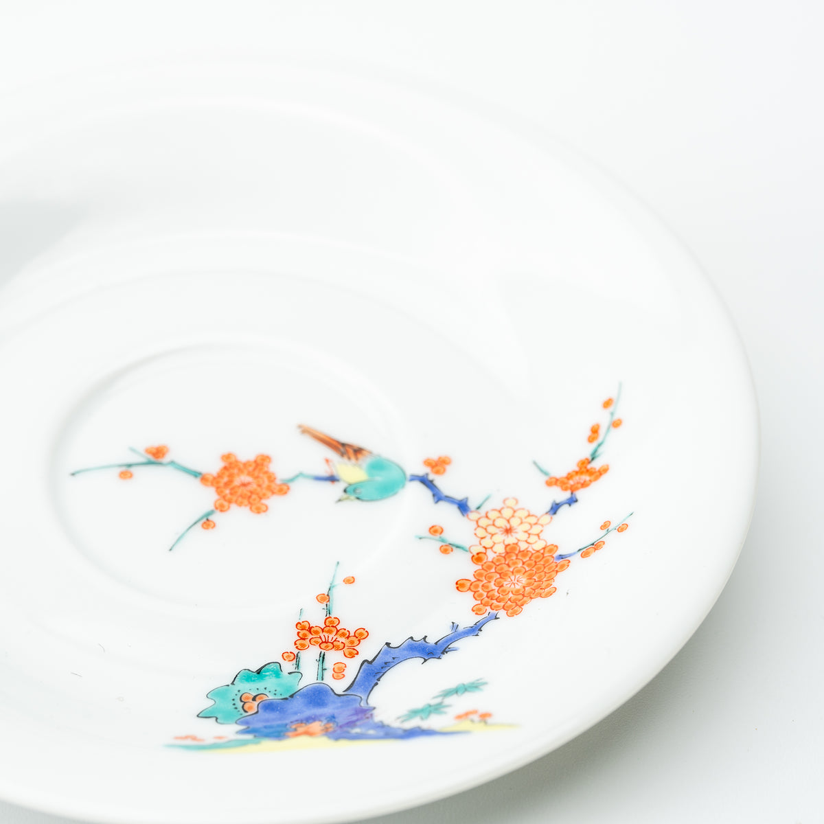 Angled view of the white plum blossom saucer with an orange flowering branch and a small turquoise bird.