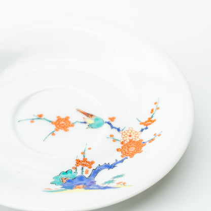 Angled view of the white plum blossom saucer with an orange flowering branch and a small turquoise bird.