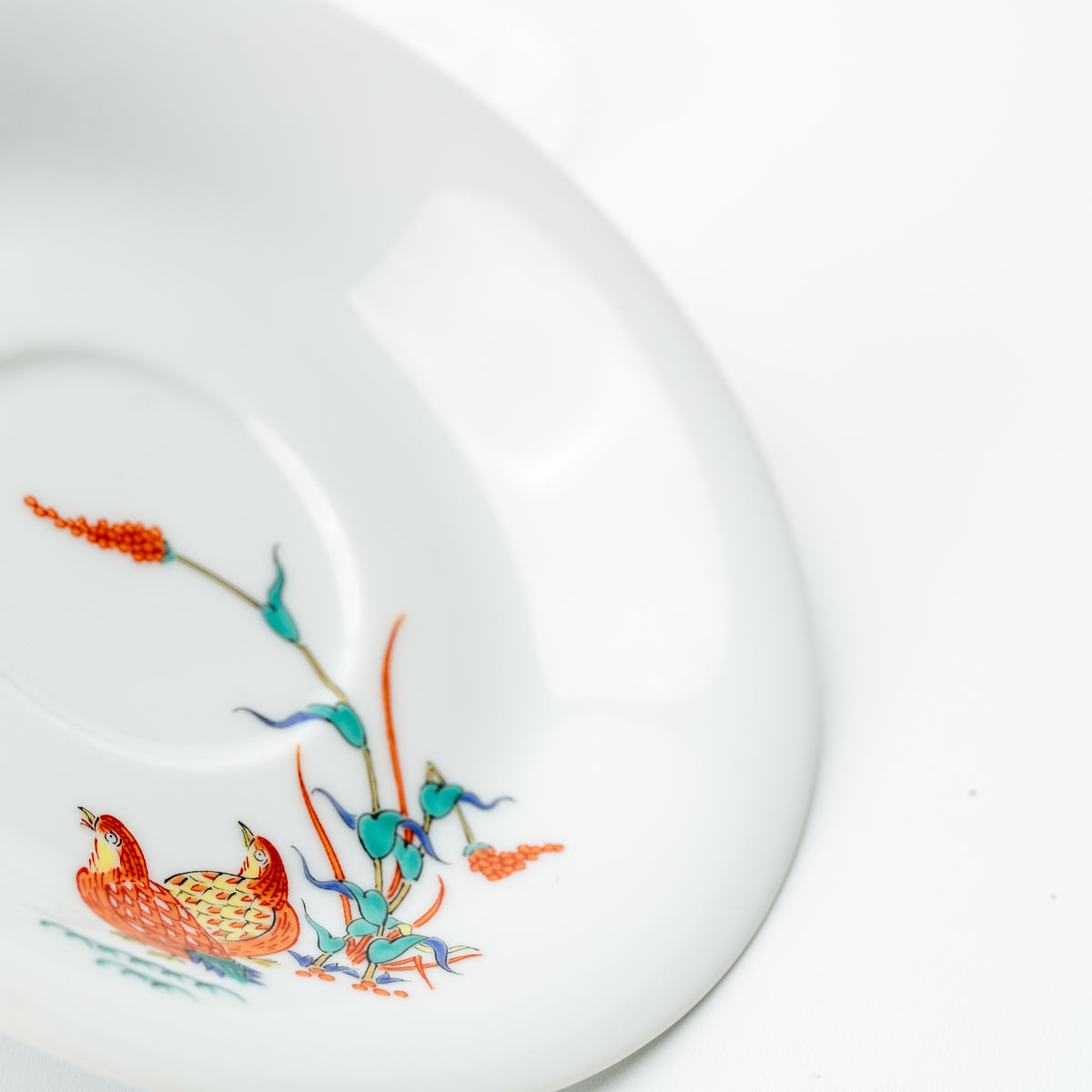Detail of the white Kakiemon-style saucer with two quail beneath orange seed heads and green leaves.