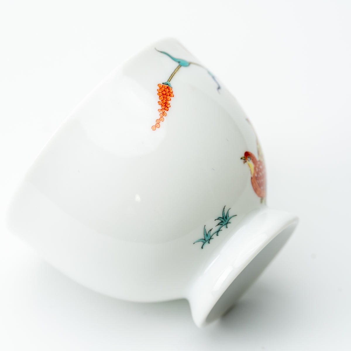 Side detail of the white quail cup, showing sparse green leaves, orange seed heads and its raised foot.