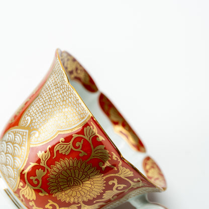 Close-up of gold-colored chrysanthemums and fine geometric panels on the red cup's flared side.