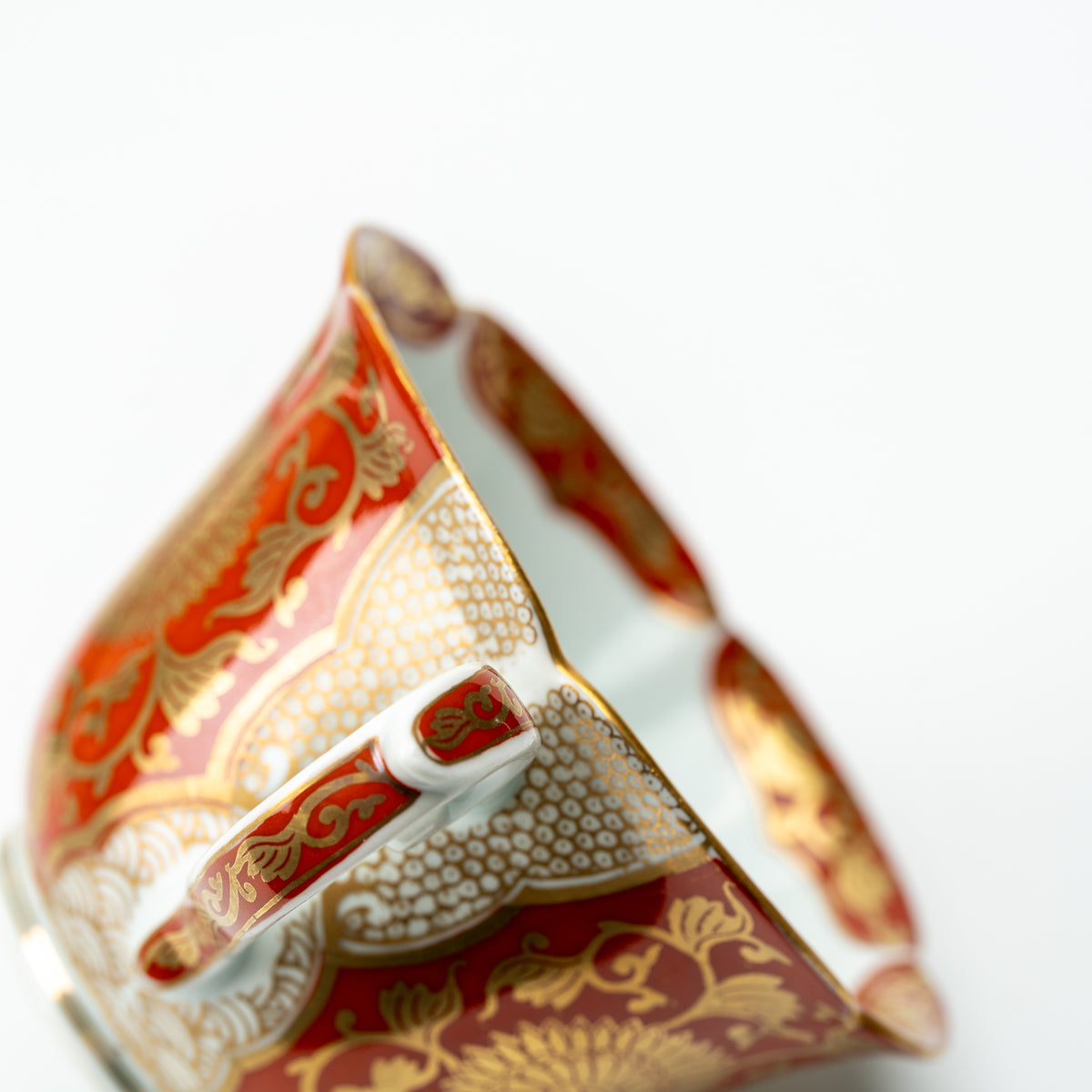 Handle detail of the red chrysanthemum cup, with gold-colored scrollwork and a scalloped rim.