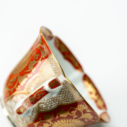 Handle detail of the red chrysanthemum cup, with gold-colored scrollwork and a scalloped rim.