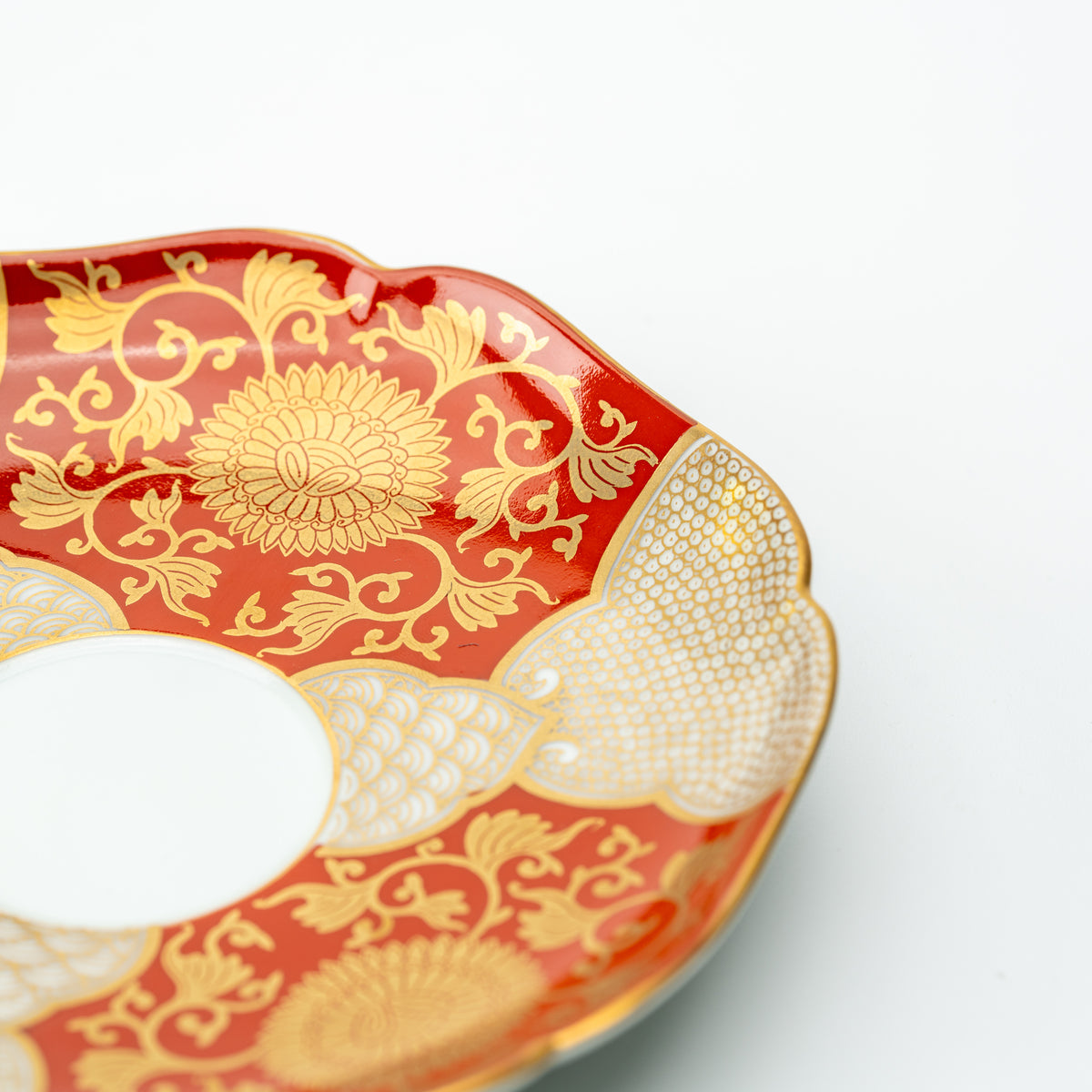 Angled close-up of the red chrysanthemum saucer with gold-colored flowers, scrollwork and patterned panels.