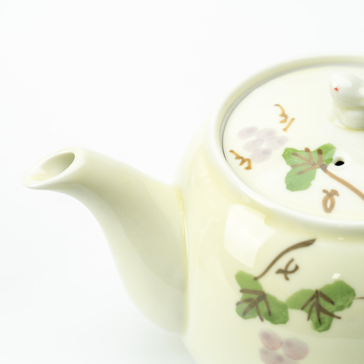 Close-up of the grape-patterned teapot's curved spout and fitted lid with green leaves and pale purple grapes.