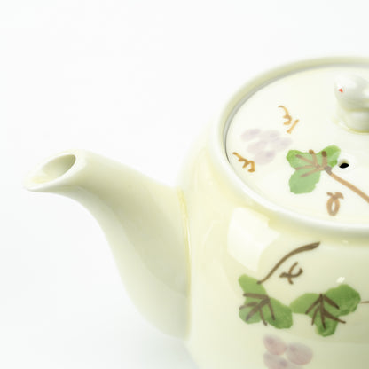 Close-up of the grape-patterned teapot's curved spout and fitted lid with green leaves and pale purple grapes.