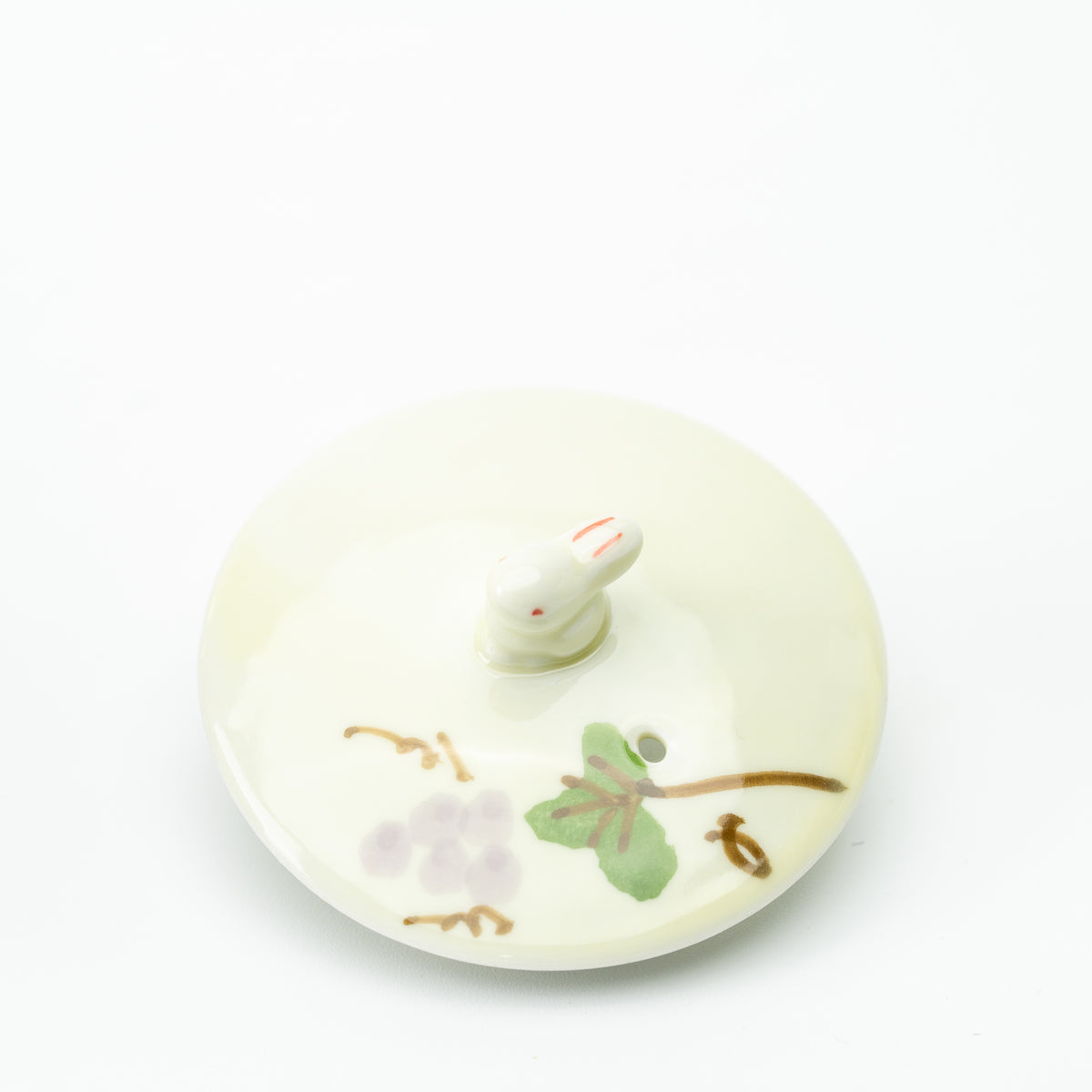 Detached teapot lid with a small rabbit-shaped knob and grape-and-leaf decoration.