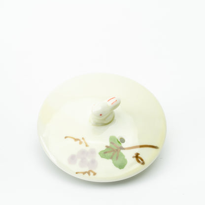 Detached teapot lid with a small rabbit-shaped knob and grape-and-leaf decoration.